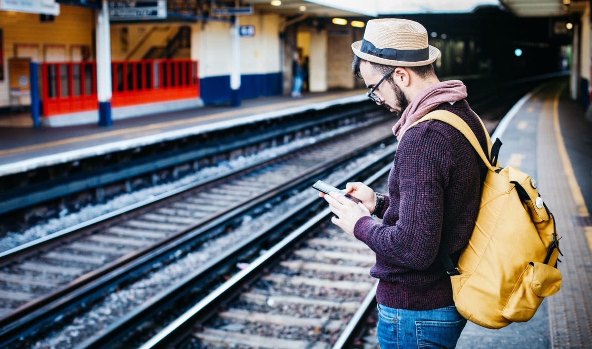 Our Ultimate Pre-Travel Checklist: Must-Dos & FAQs For Your International Trip 19 A man with a backpack and hat waiting on a train station platform.