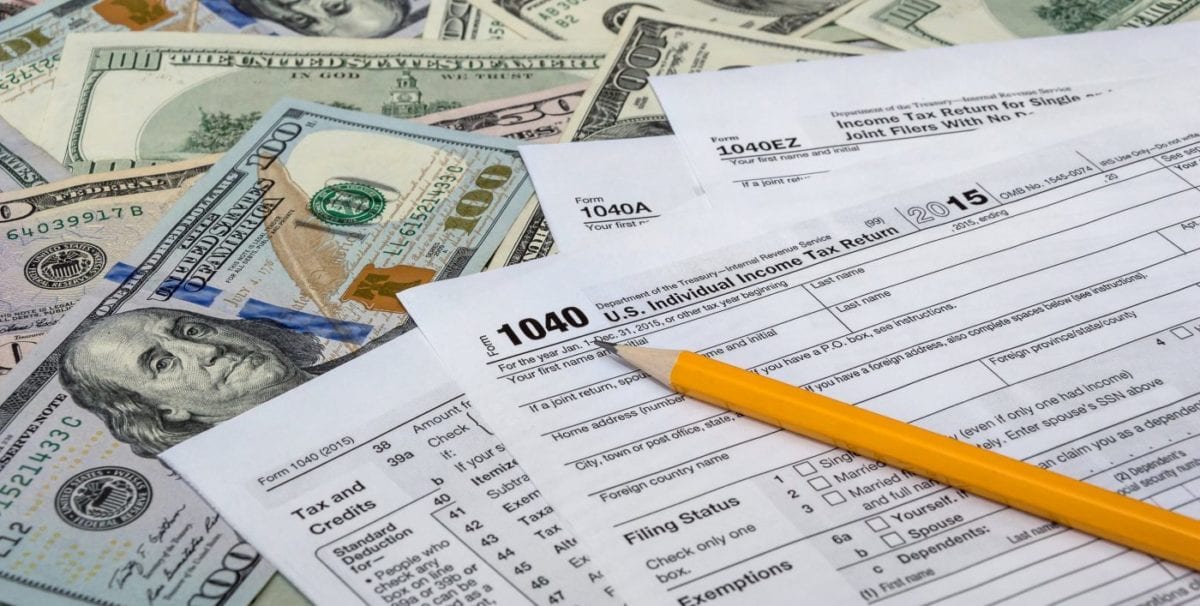 Tax Form 1040 with a pile of U.S. Dollars and a pencil.