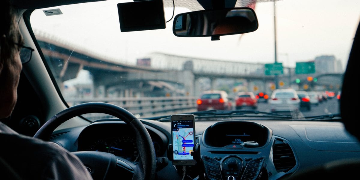 We've Had It: Amex Card Credits & Benefits Are Out of Control 1 The front seat of a car with a driver in traffic getting help help from phone navigation.