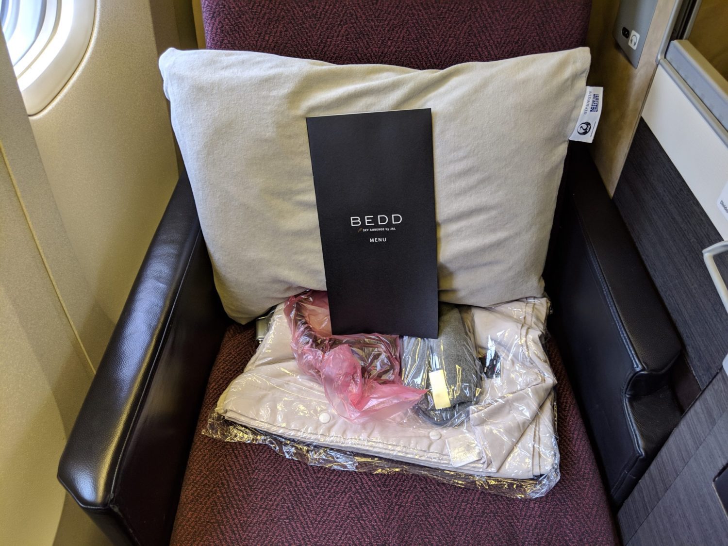 a pillow, menu, headphones, slippers, and duvet sitting on a business class seat
