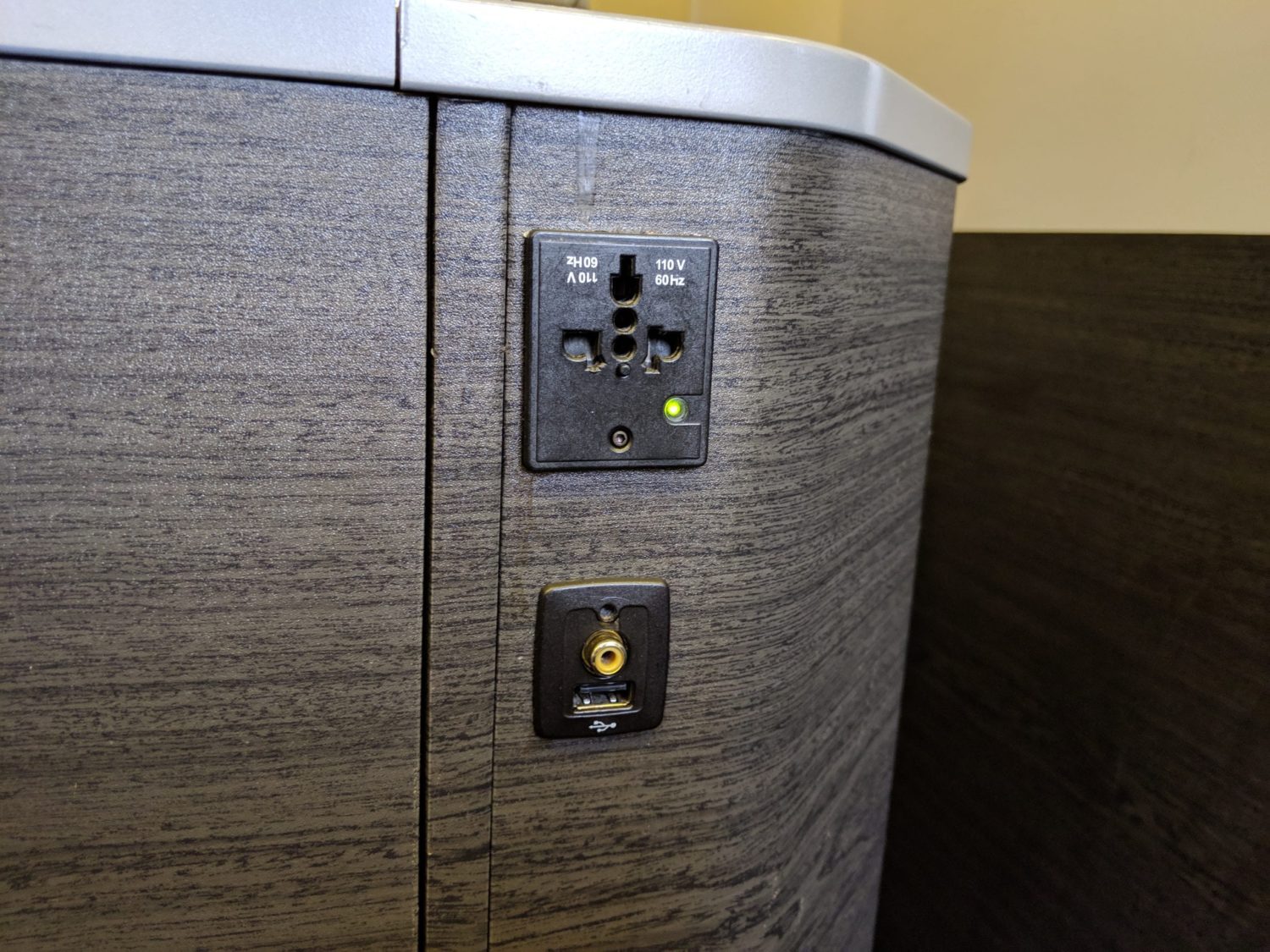 a universal power socket and usb charging on a woodgrain console wall of a business class seat