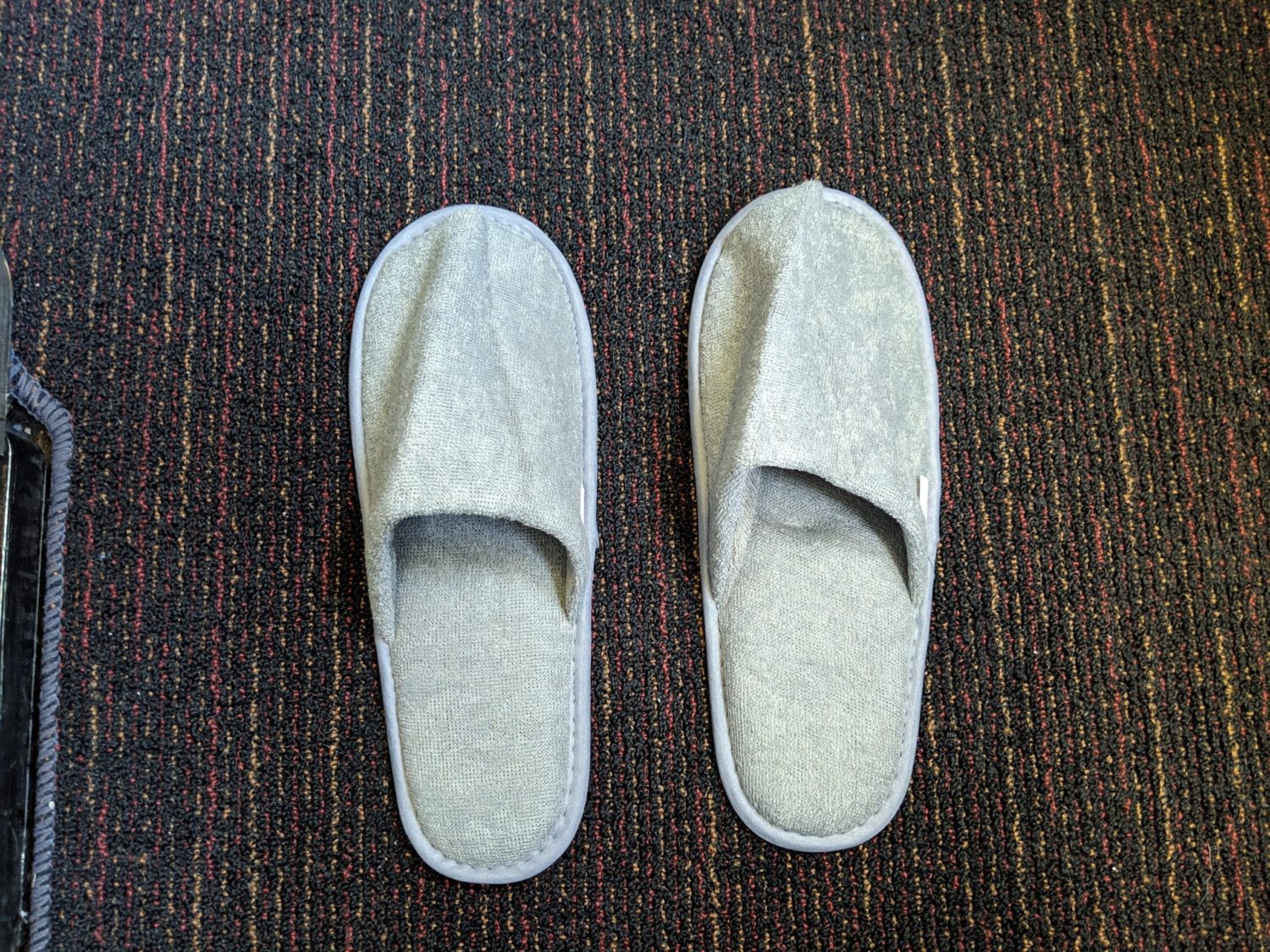 a pair of gray slippers sitting on a red and black carpet