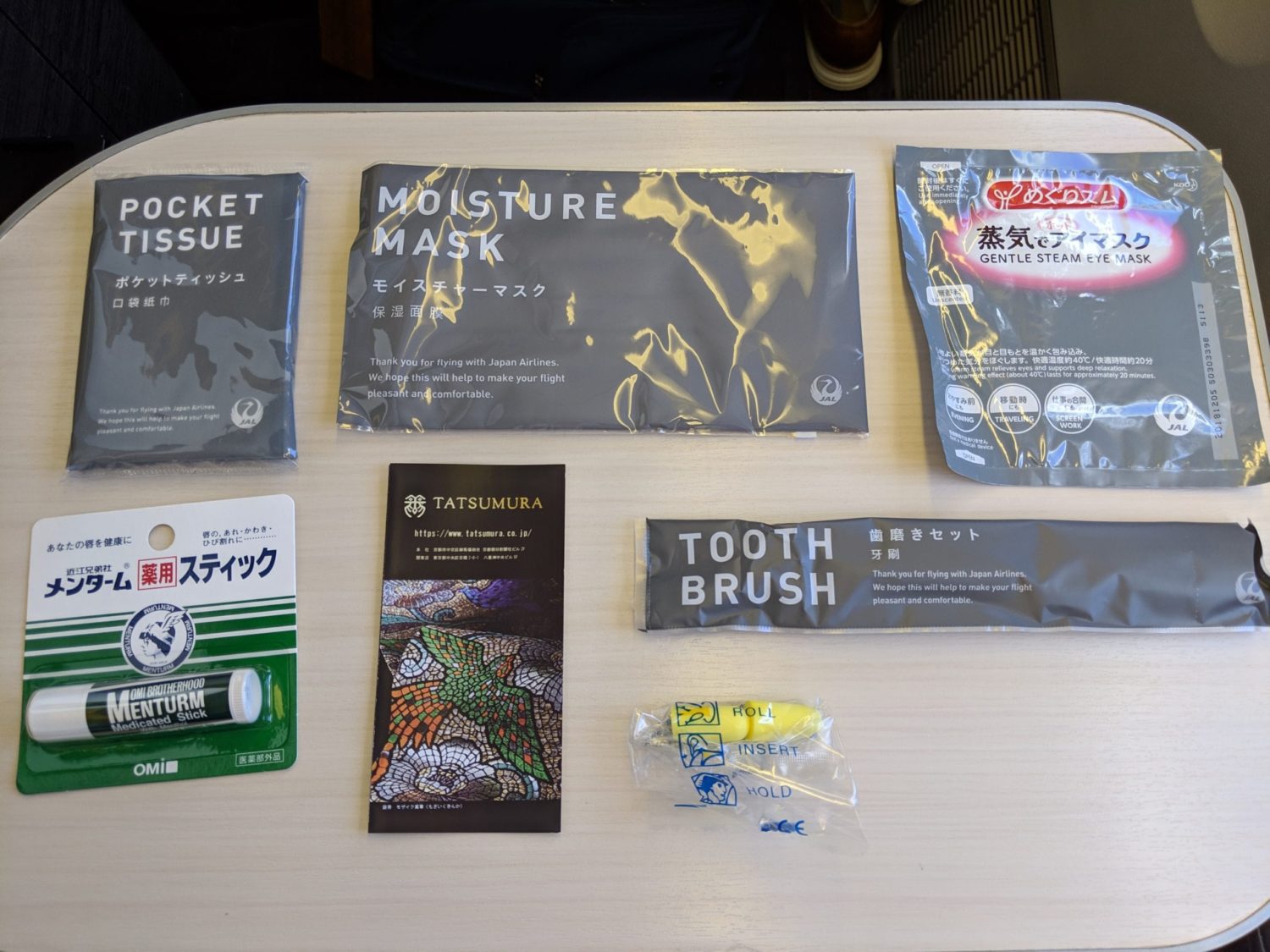 a package of tissues, moisture and steam eye mask, medicated stick, toothbrush, and ear plugs all sealed in plastic