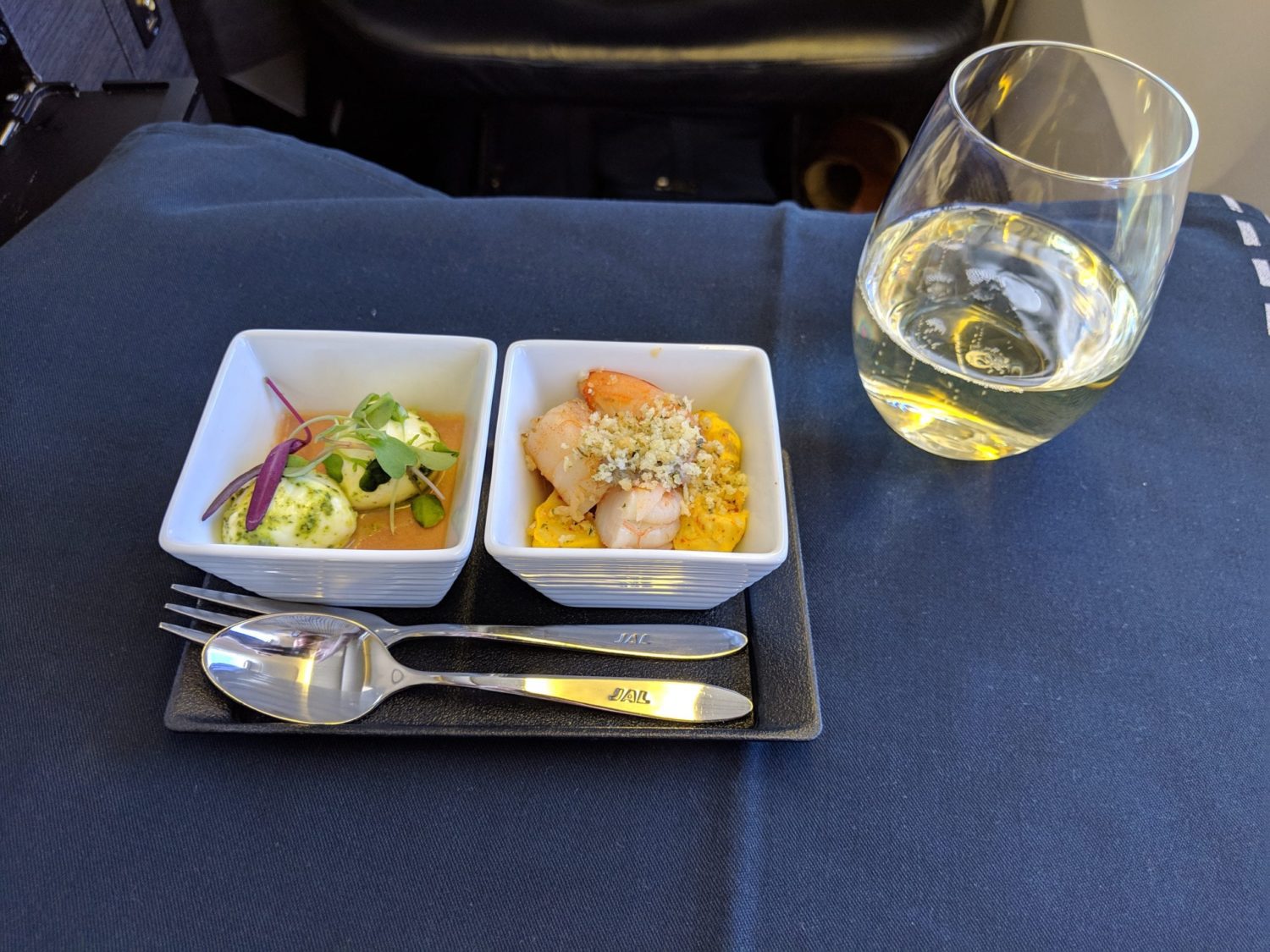 a small tray with two containers of food and a glass of champagne