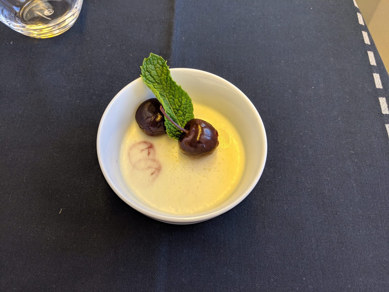 a small bowl of custard topped with two cherries and a green sprig of mint