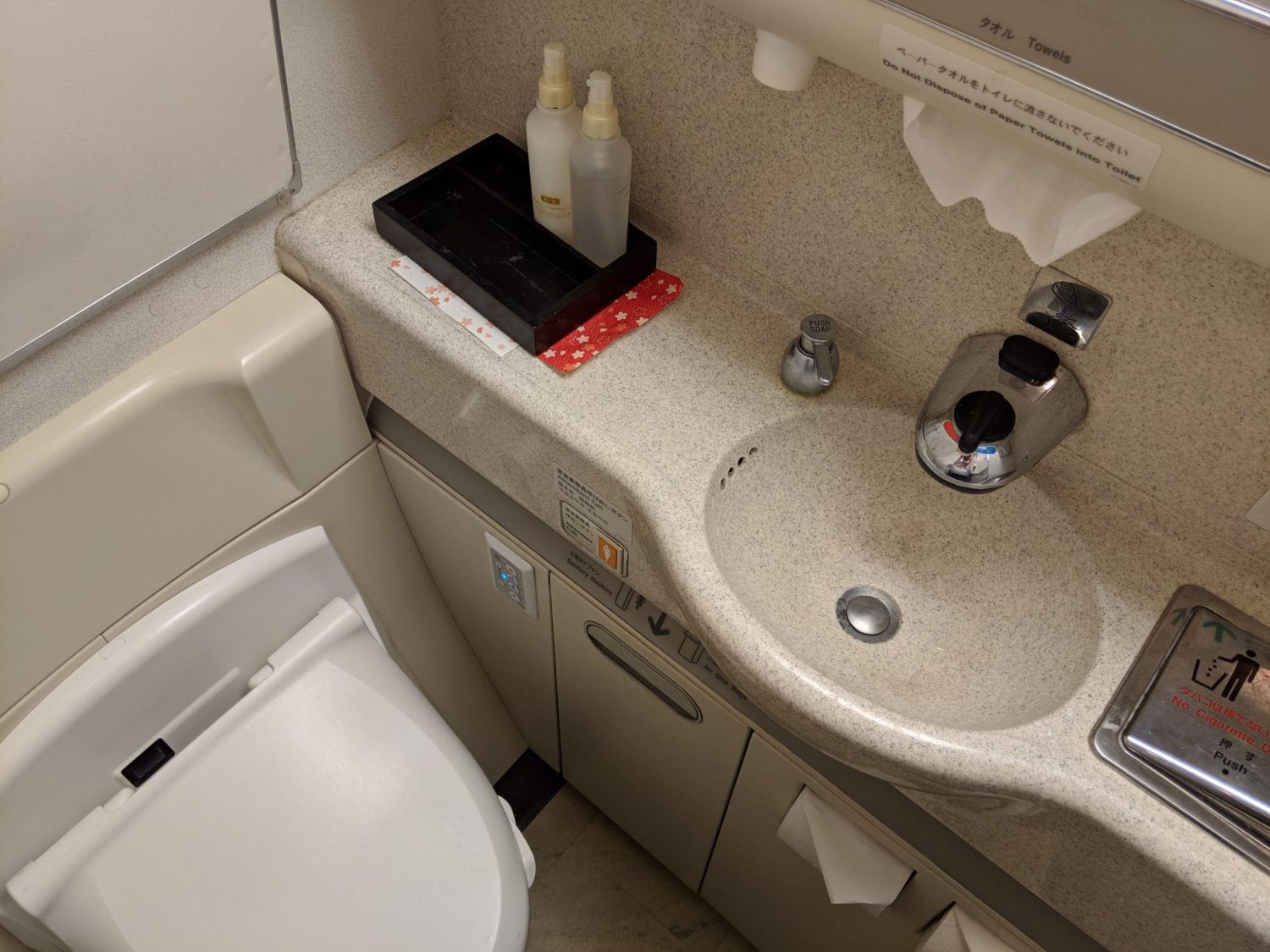 an airplane lavatory with toiletries on the counter and a bidet function