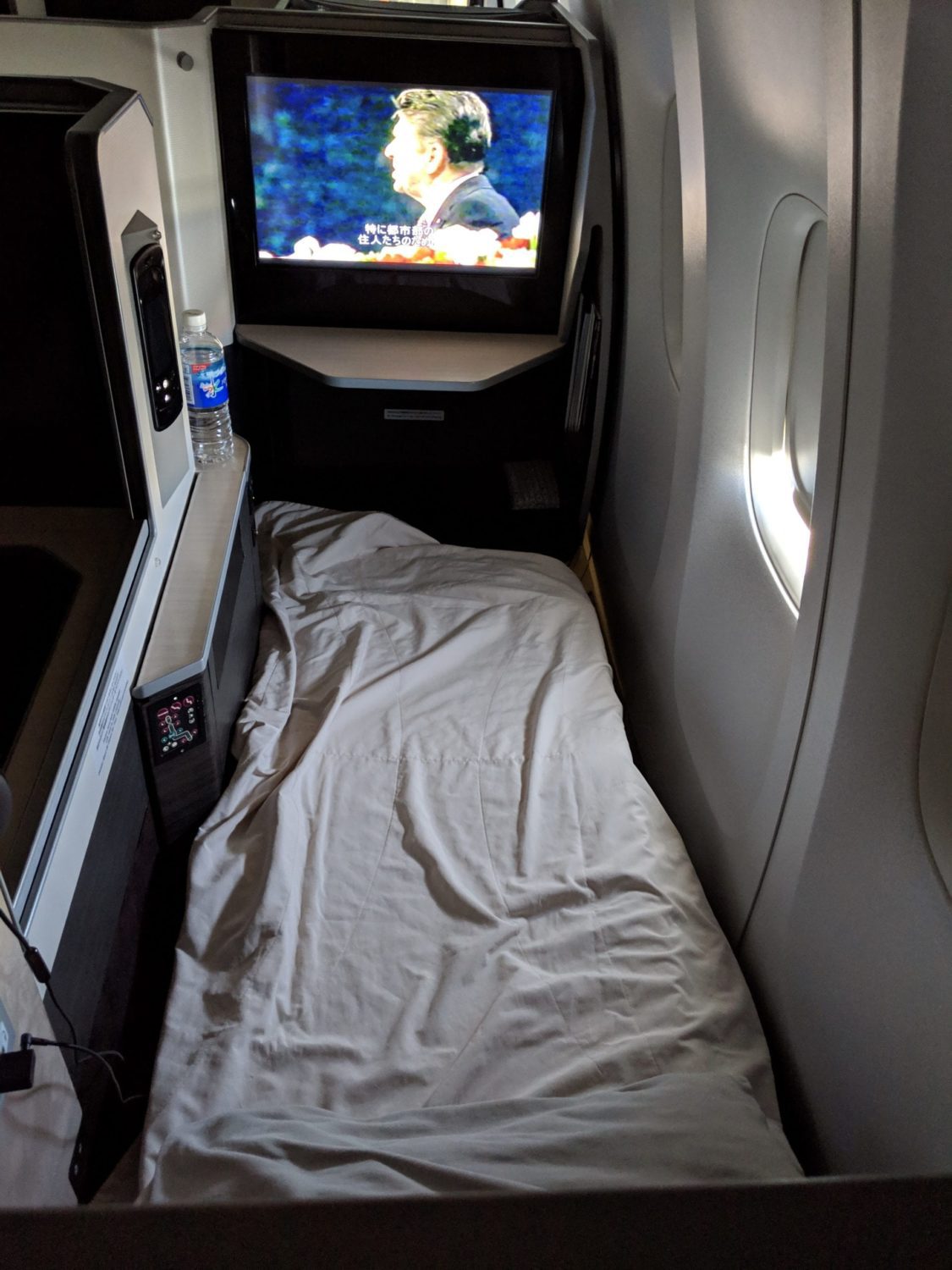 a business class bed covered in a duvet with a movie playing