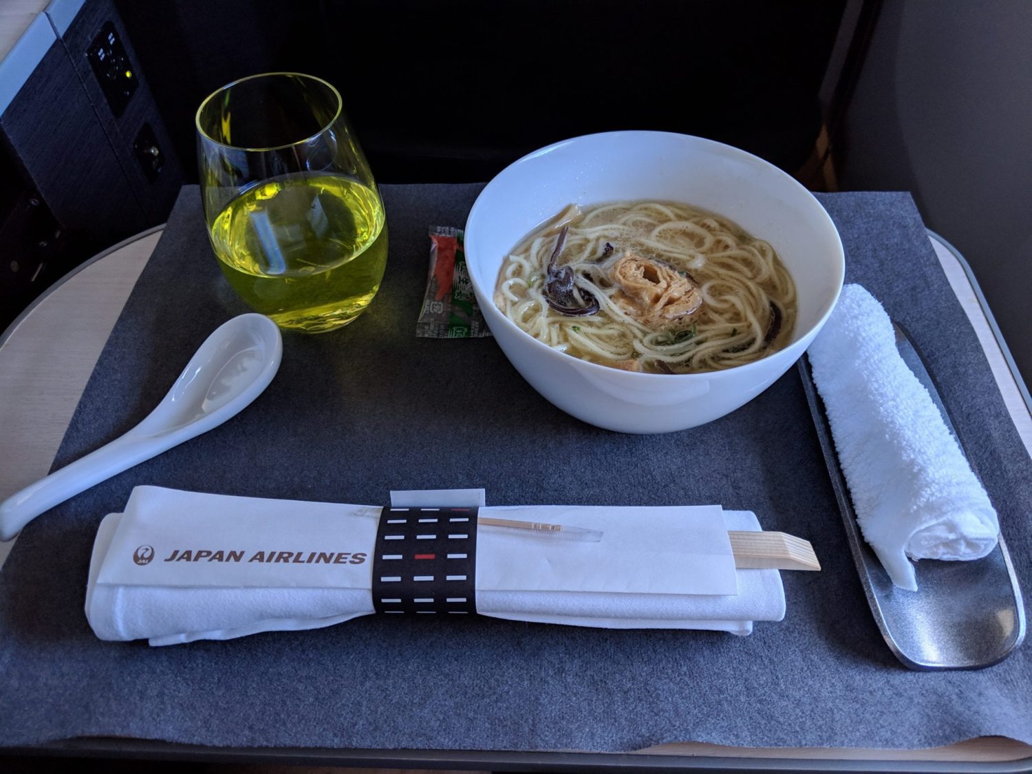 a bowl of ramen on an airplane tray with a green drink next to it