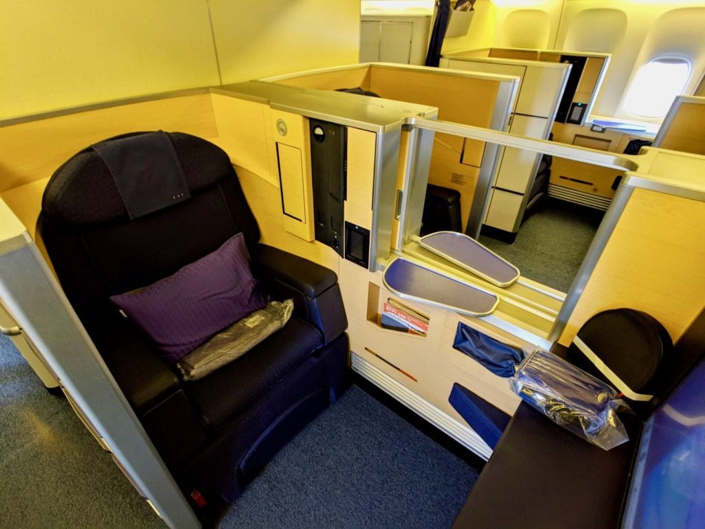 a purple first class seat with light wood walls. A divider separates the two seats. 