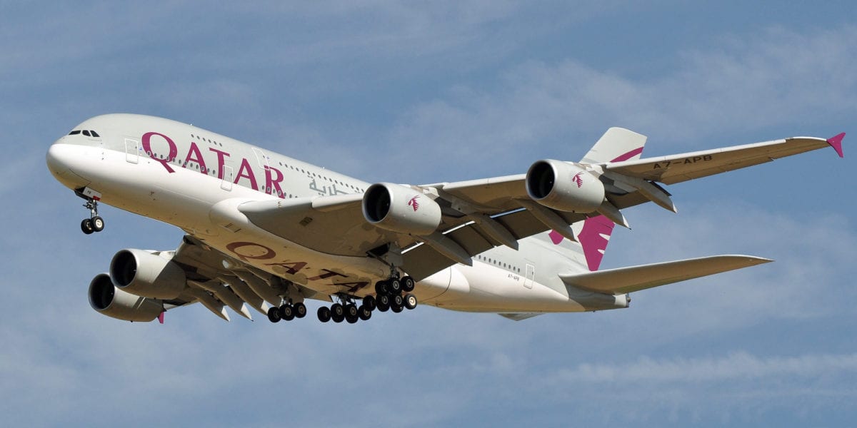 A large Qatar passenger jet flying through a cloudy blue sky