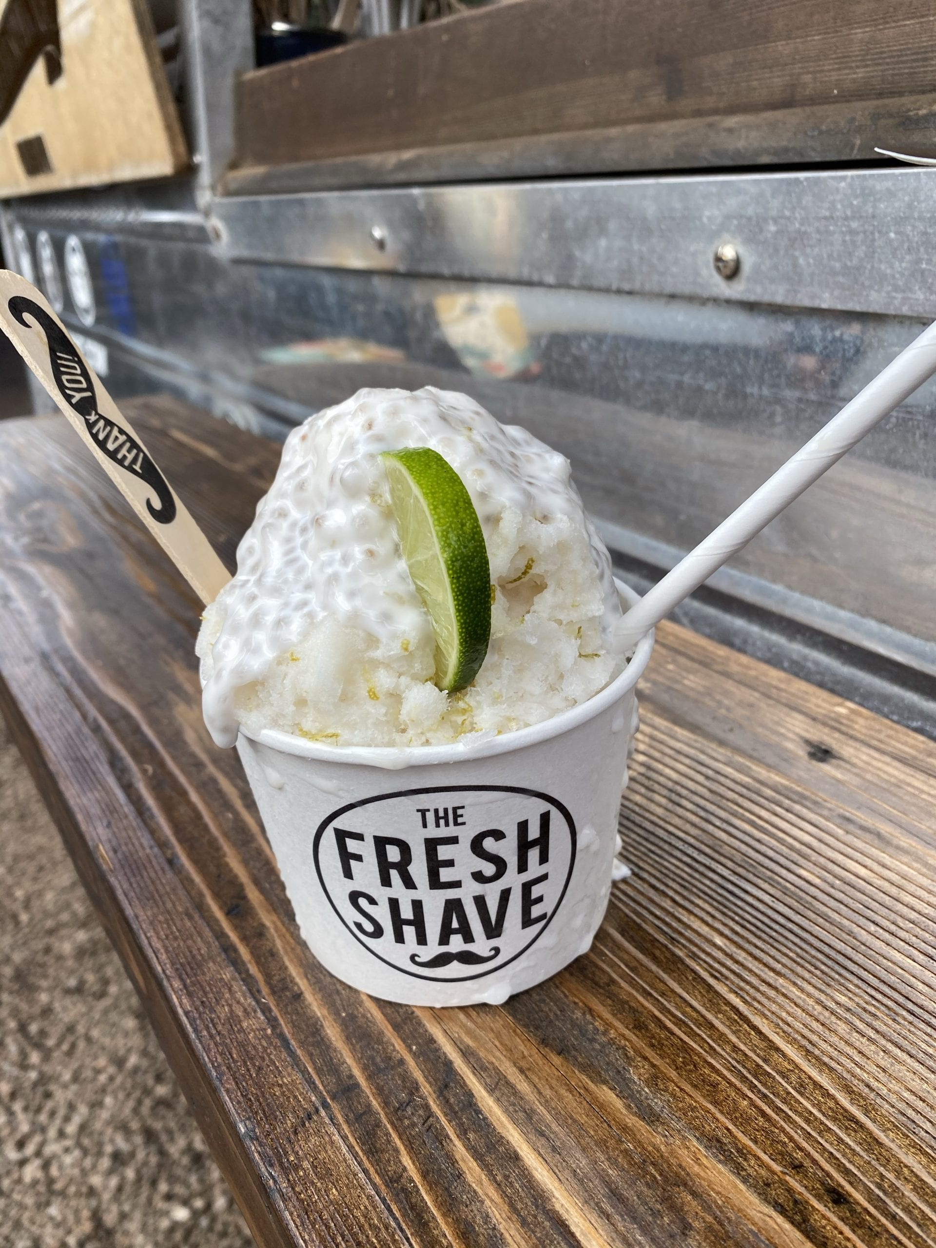 shaved ice with a lemon and coconut topping in a small paper bowl that reads "the fresh shave"