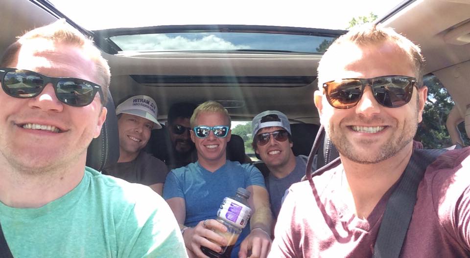 A group of people wearing sunglasses posing for the camera, in a car