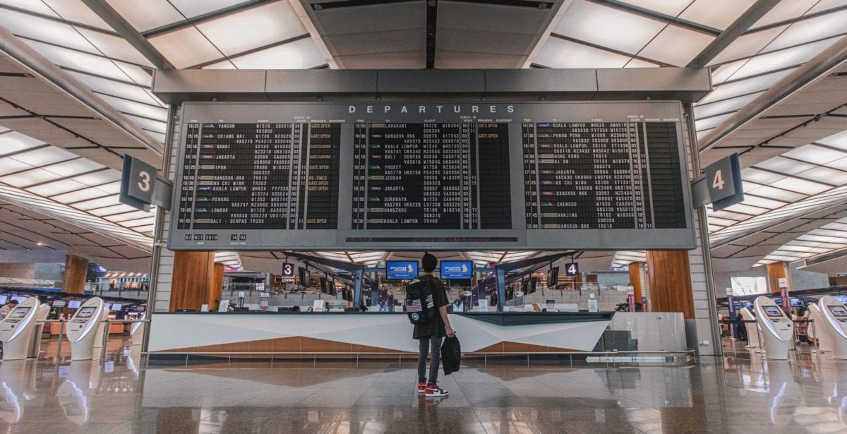 Is It Cheaper to Fly Nonstop or With a Layover? 1 a person standing in front of an airport departures board