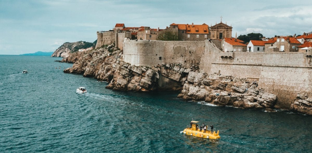 A stone bridge over a body of water with Dubrovnik in the background