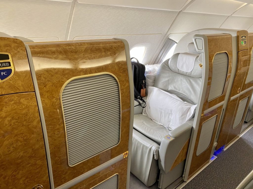 emirates first class seat on the airbus a380 with a backpack by the window.