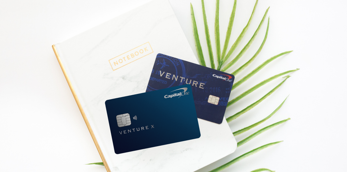 Capital One Venture and Venture X credit cards on top of a notebook with a palm leaf in the background.