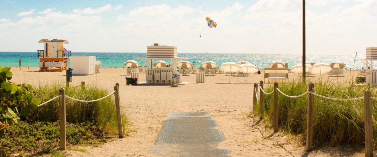 a sand-covered sidewalk leading to a sandy beach in florida. the beach has lifeguard towers and lots of beachgoers.