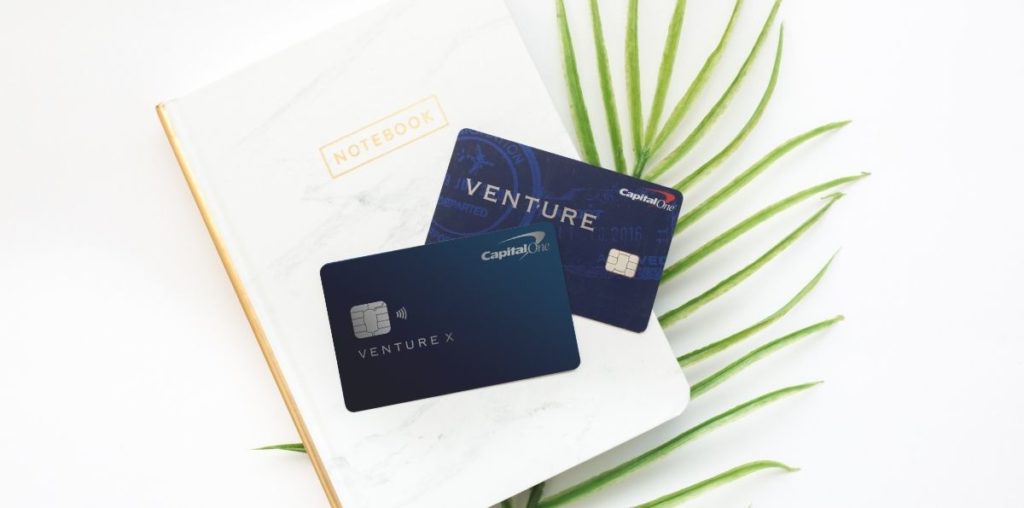 capital one venture and venture x credit cards sitting on a notebook with a palm leaf.