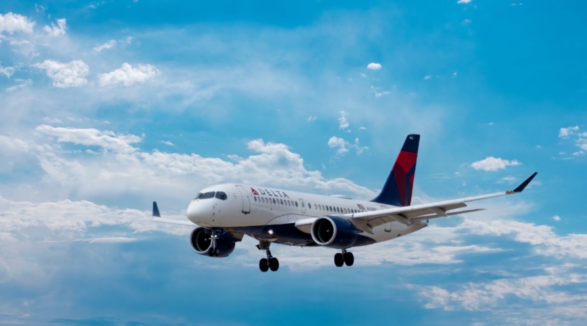 A large delta passenger jet flying through a cloudy blue sky
