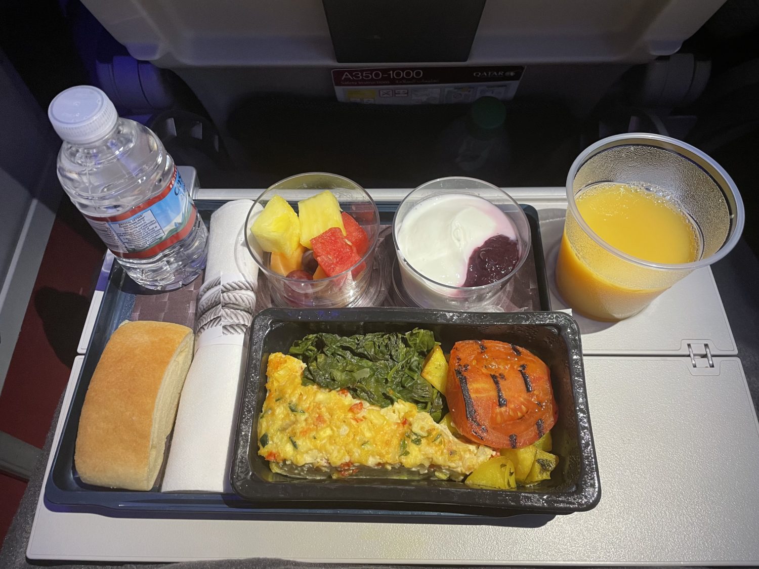 a tray of breakfast with fruit and yogurt on an airplane tray table