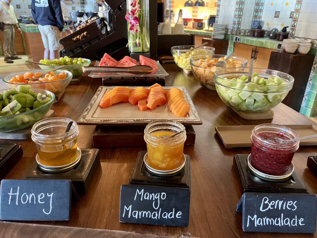 several jars of jam and marmalade with platters of fruit in the background