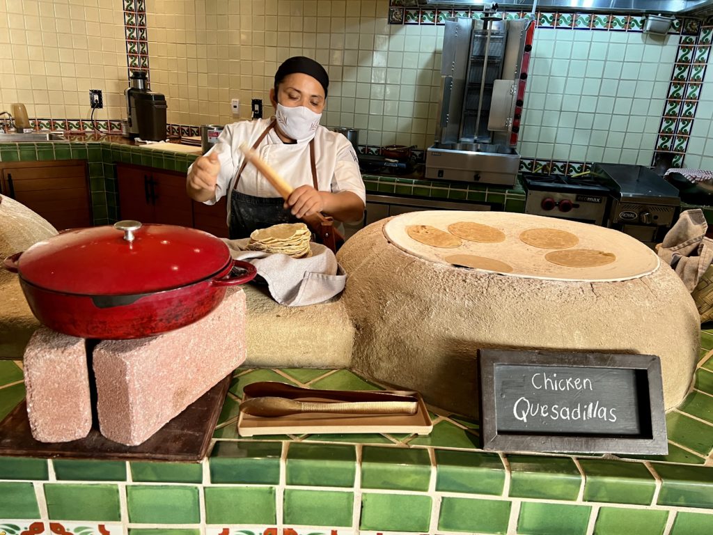 a woman making tortillas fresh on a round stone