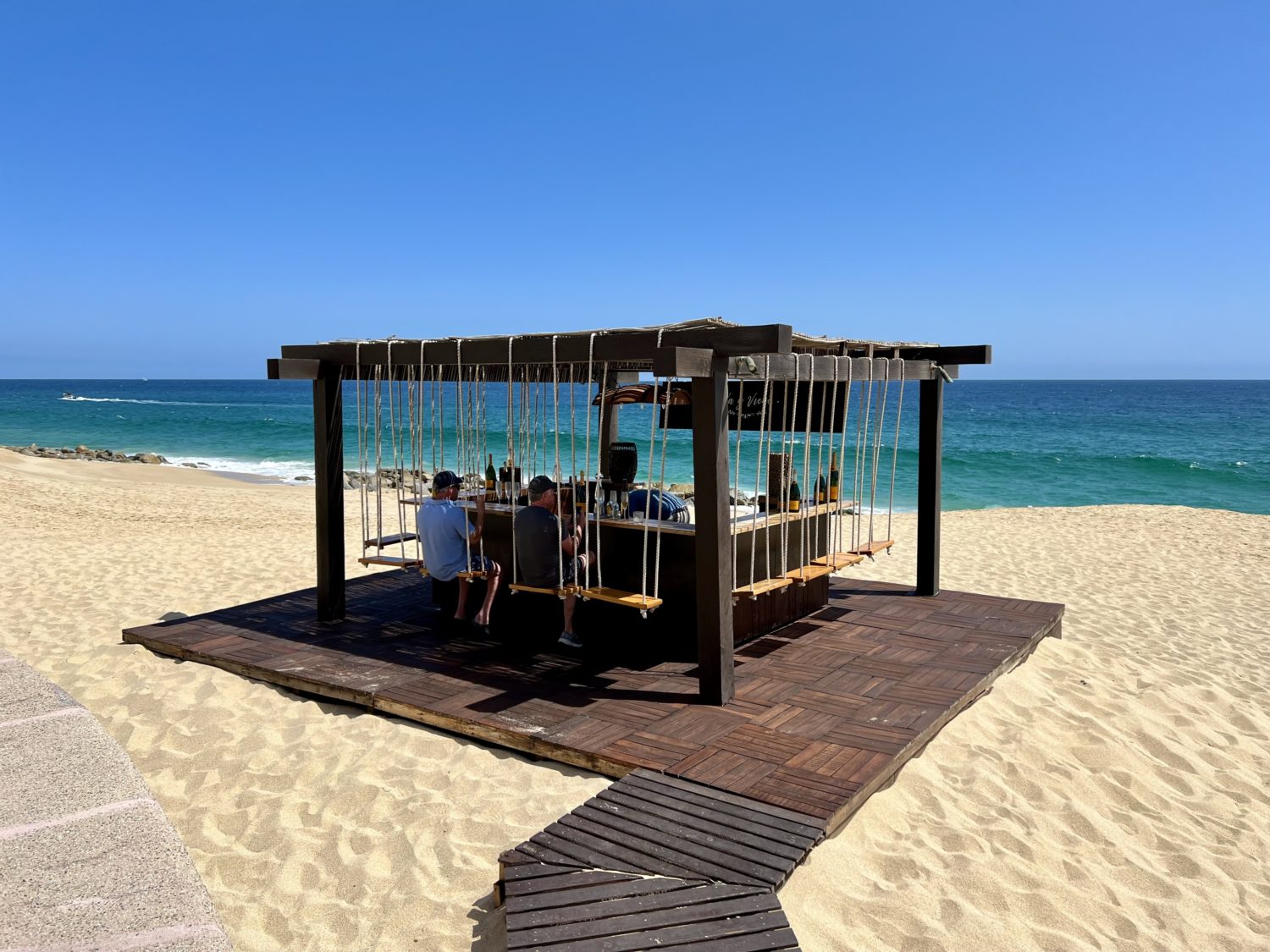 a small beach bar with swinging chairs with the ocean behind it