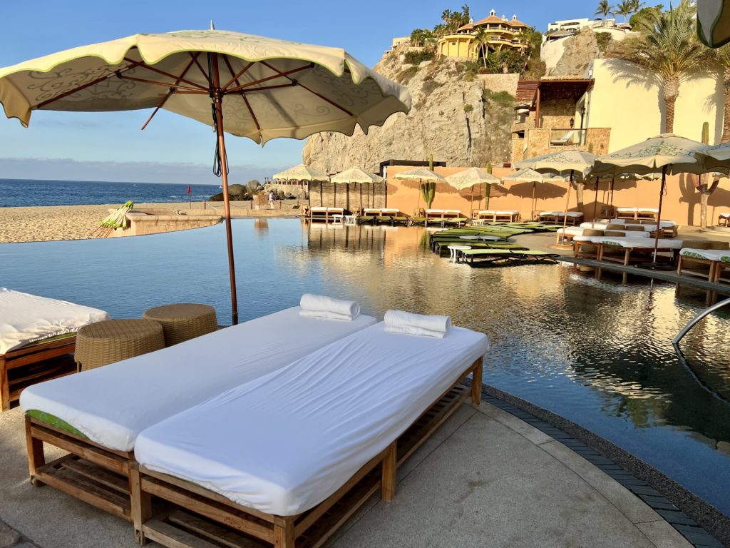 white cushioned pool chairs surrounding a glassy pool