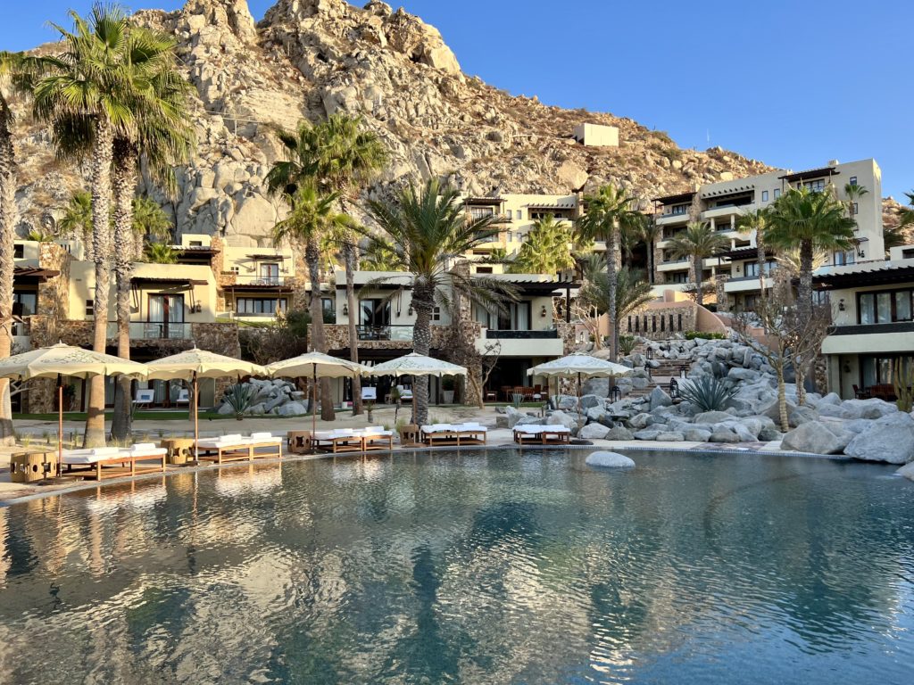 a pool surrounded by beach chairs and villas on the hills behind them