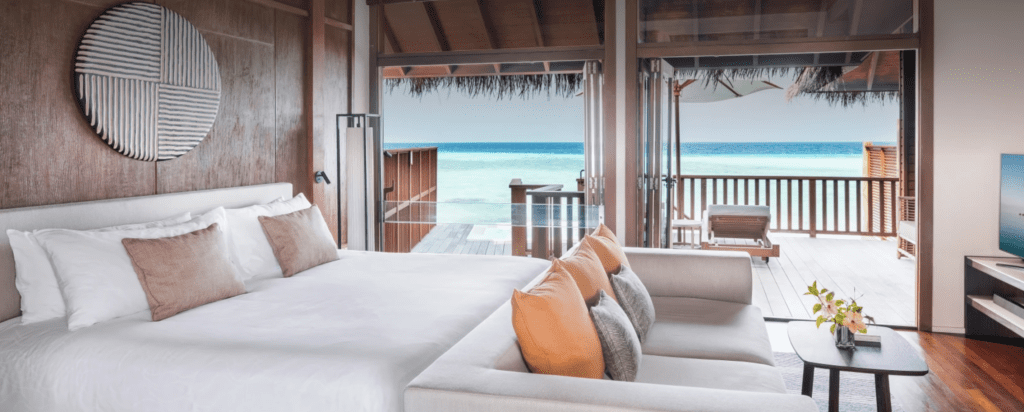 a large bed with a loveseat in front of it with the ocean out the windows