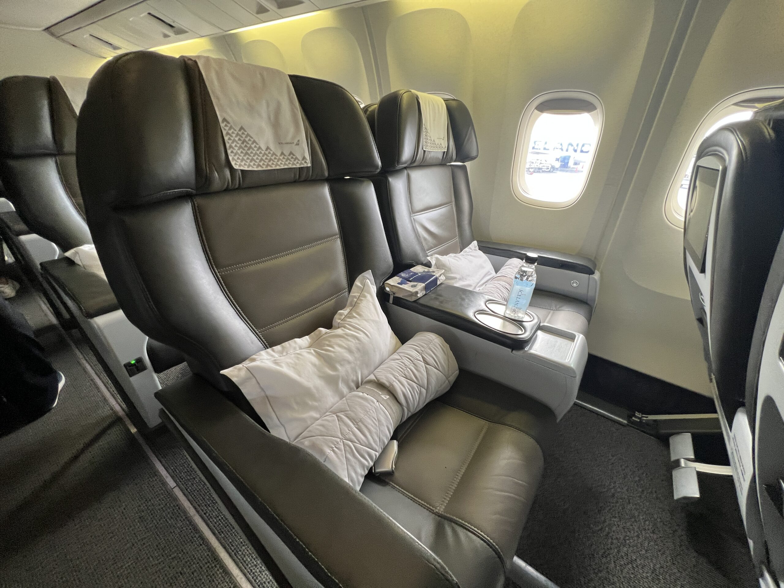 Two business class seats. Each seat has a pillow, rolled-up blanket and a water bottle. 