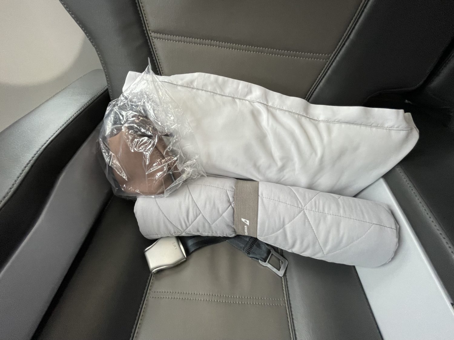 A blanket, amenity kit, and pillow on an airplane seat. 