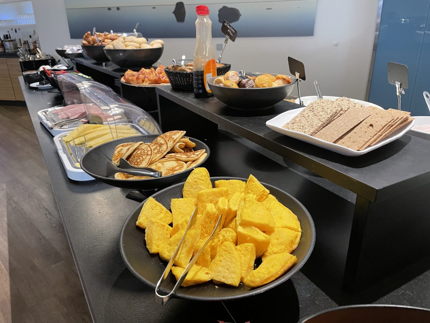 a breakfast buffet of bread, crackers, pancakes, meat and cheeses