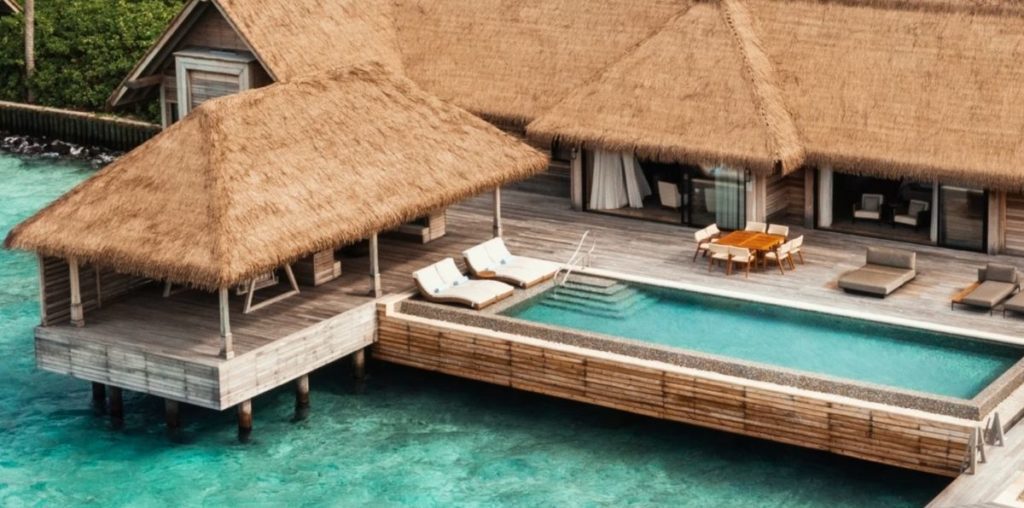 a large villa with a straw thatched roof perched over the ocean with a long lap pool