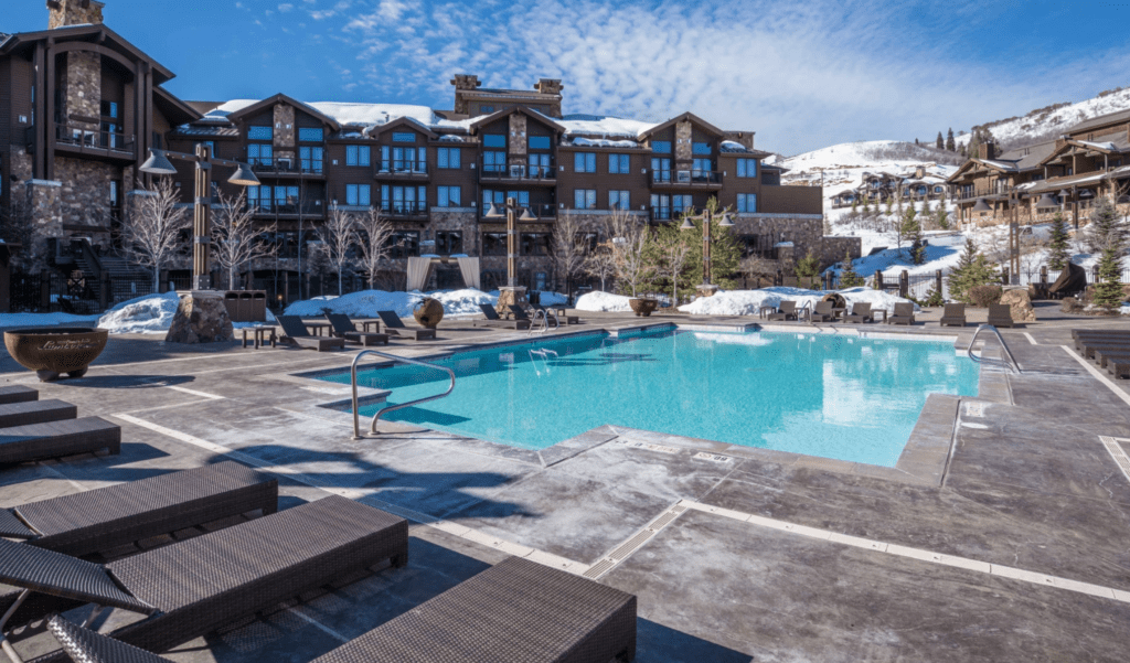 a pool surrounded by deck chairs with snow-capped structures in the background