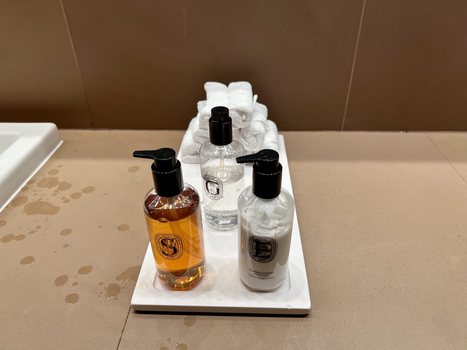 three bottles of diptyque amenities and a tower of cloth hand towels