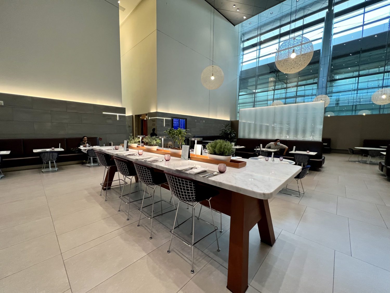 long dining table with wire metal chairs and circular light fixtures overhead