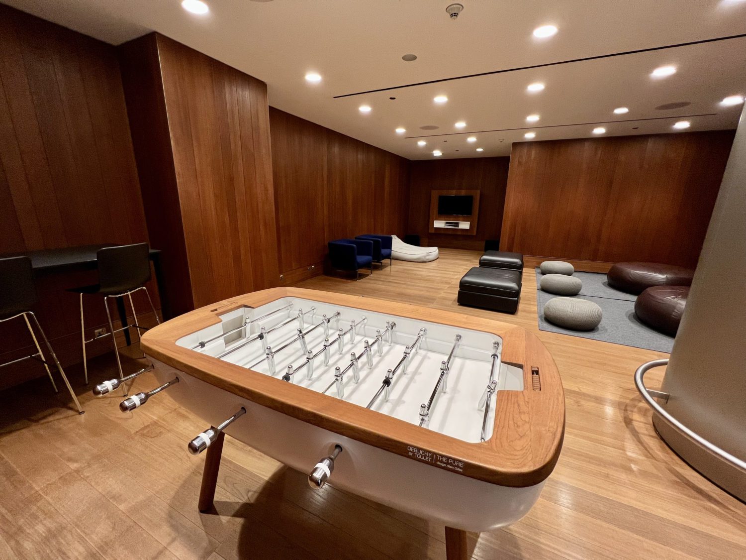 wooden foosball table with seating poufs and chairs in the background