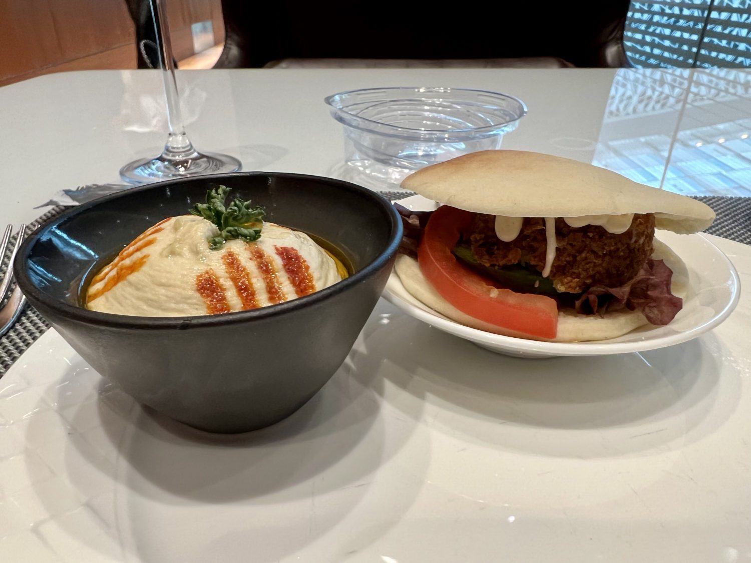 a small container of hummus and a falafel inside a pita with tomato