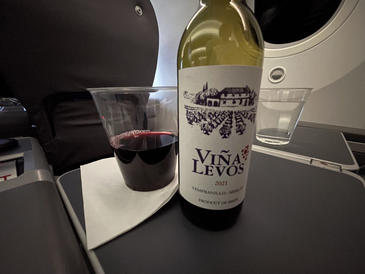 A cup and bottle of red wine on an airplane tray
