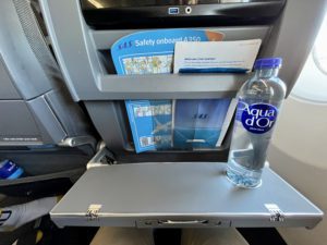A tray table pulled halfway open on an airplane with a bottle of water on it. 