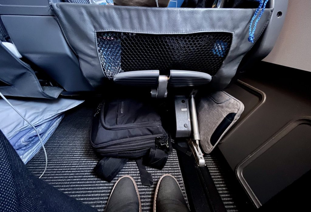 a backpack stored underneath an airplane seat