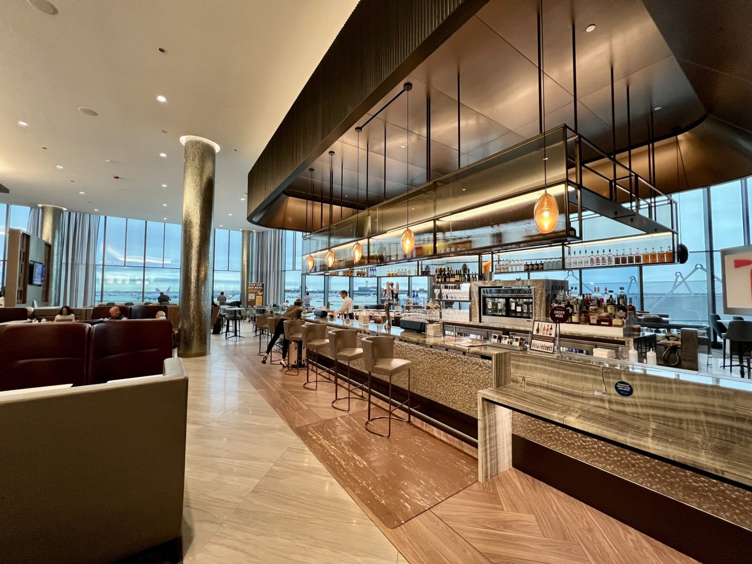 a long bar with high ceilings inside an airport lounge