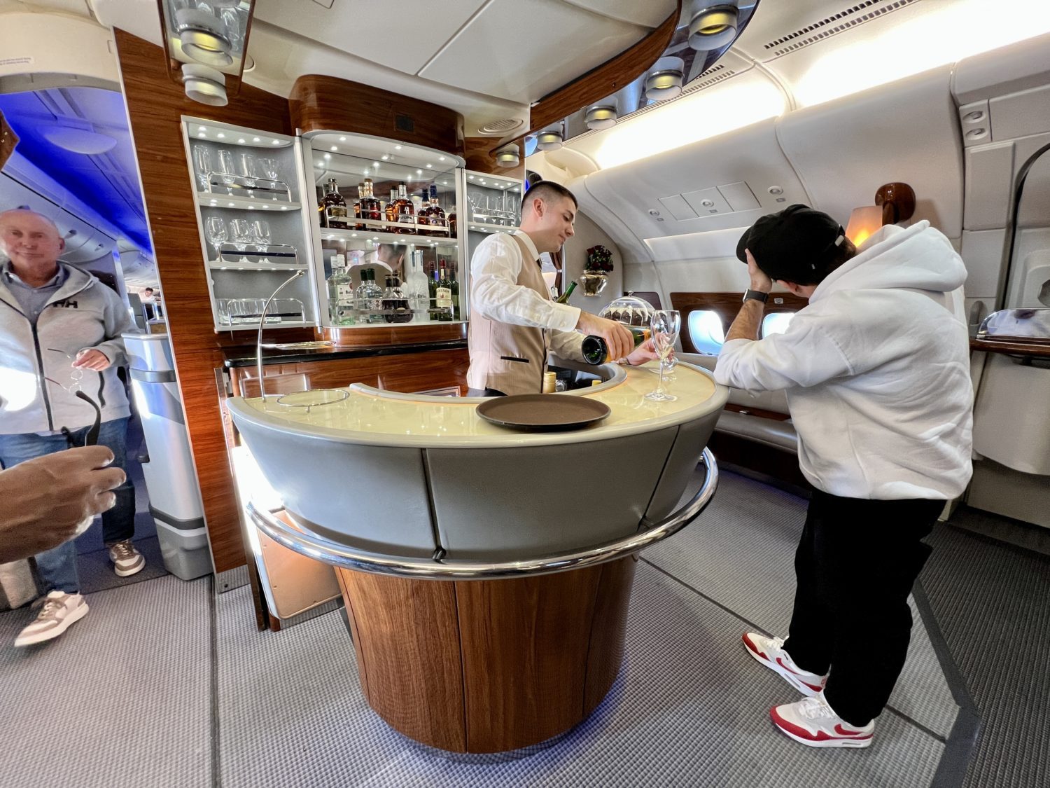 a bartender pouring a glass of champagne for a passenger leaning on the circular bar