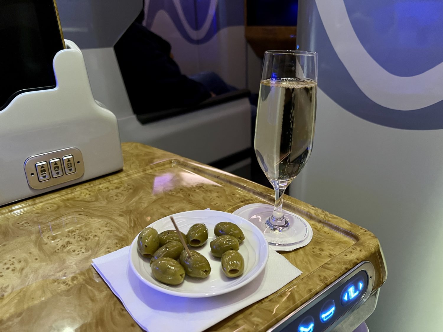 a small dish of green olives with a toothpick and a glass of champagne