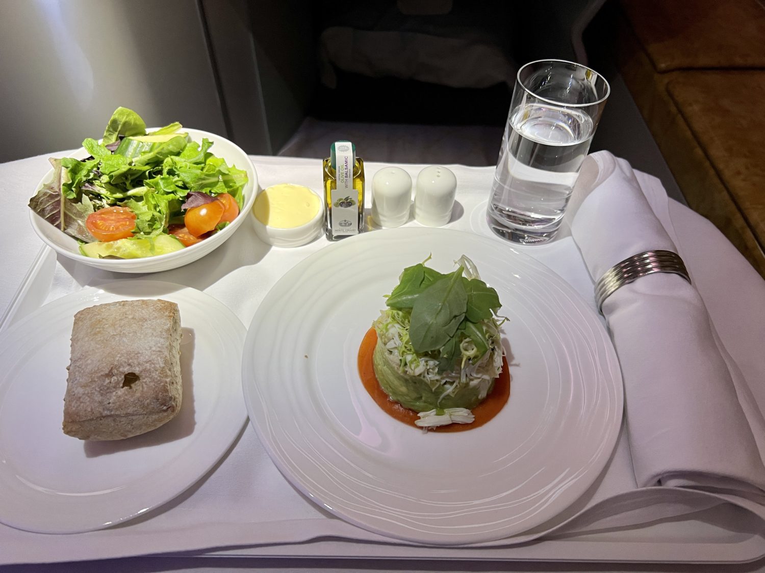 a tray table covered in cloth with a seafood dish, bread roll and salad