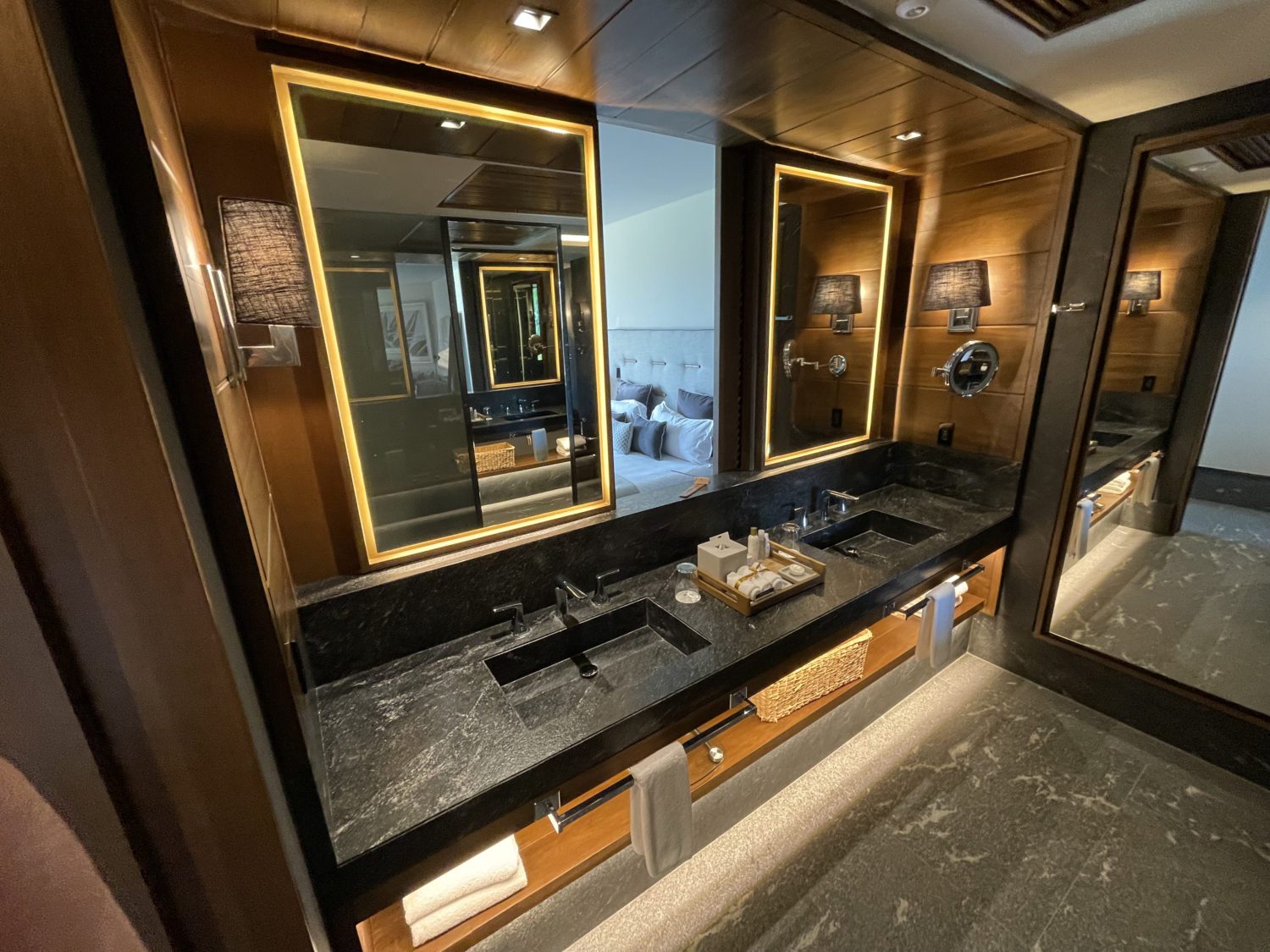 black marble bathroom vanity with a double sink, wood paneling, two backlit over-the-sink mirrors and a full length mirror. 