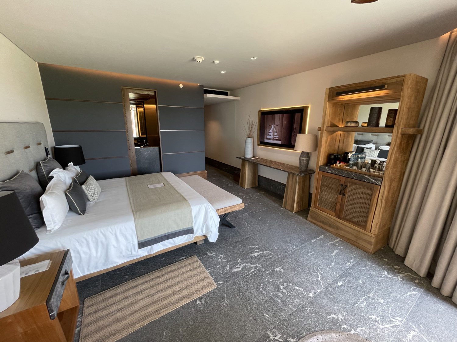 a hotel room with a king size bed, wall-mounted TV, and mini bar. 