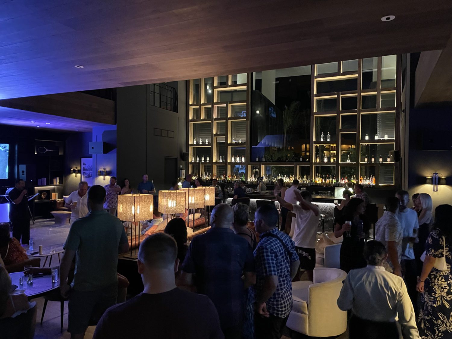 a busy, dimly lit bar with lots of patrons standing around 