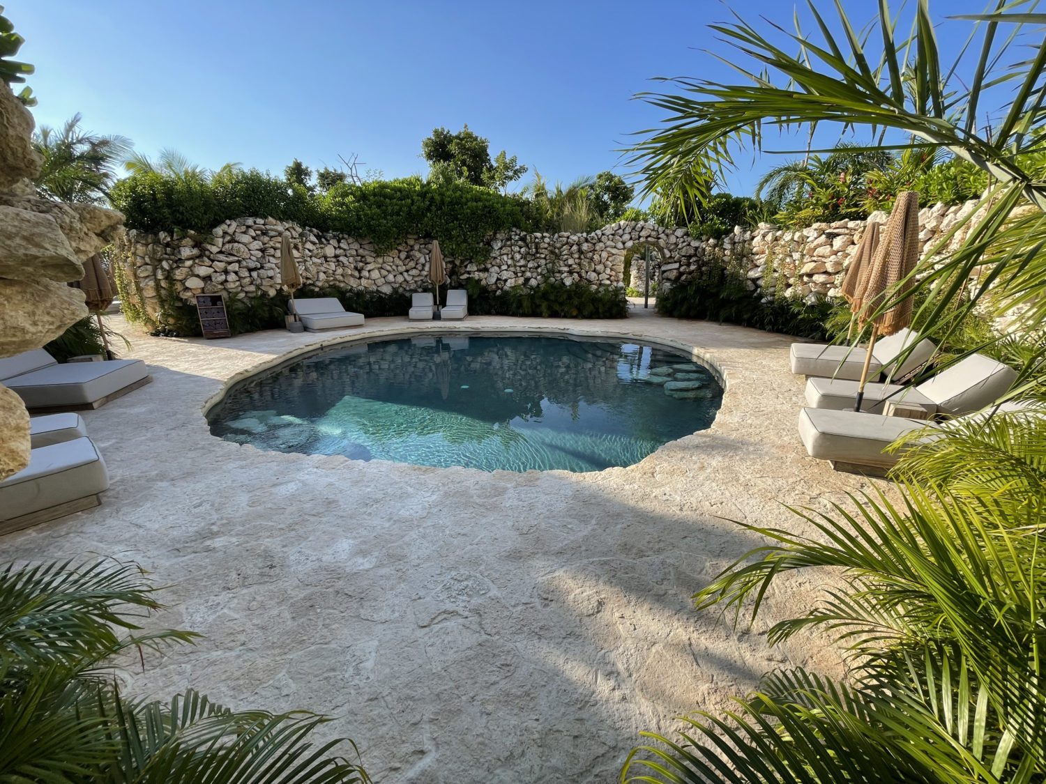 a small, circular man-made cenote pool with beach loungers surrounded by a stone wall. 